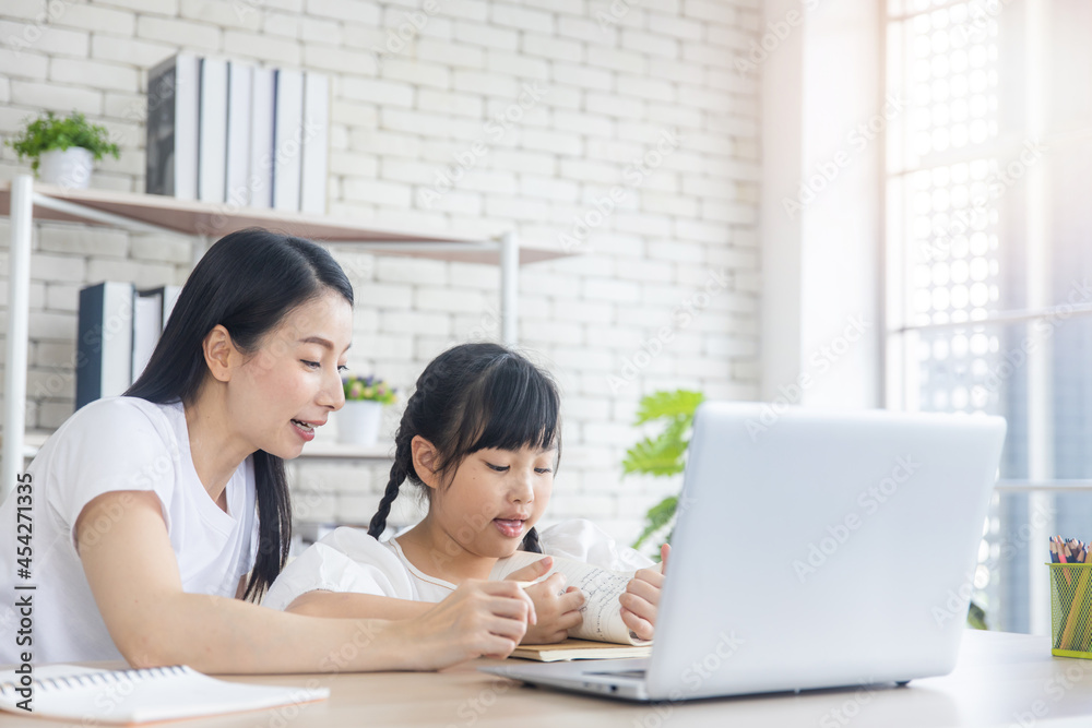 Happy young Asian mother and embracing cheerful and cute daughter watch video and learning online on laptop together, smiling mom or nanny and little girl child have fun Happy young Asian mother and embracing cheerful and cute daughter watch video and learning online on laptop together, smiling mom or nanny and little girl child have fun