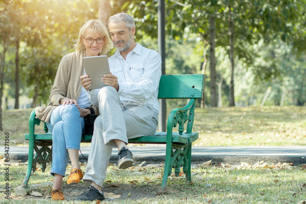 Active happy and enjoy love seniors couple sitting on bench and VDO call and use tablet in park Active happy and enjoy love seniors couple sitting on bench and VDO call and use tablet in park