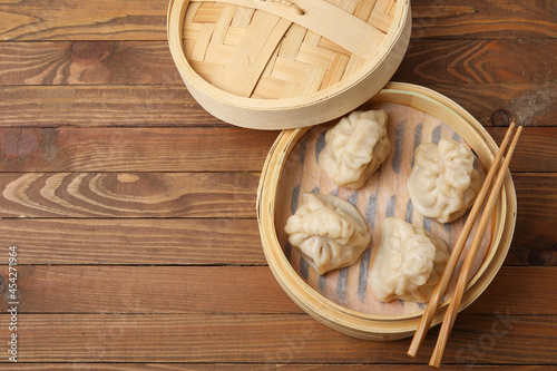 Bamboo steamer with tasty dumplings and chopsticks on wooden background