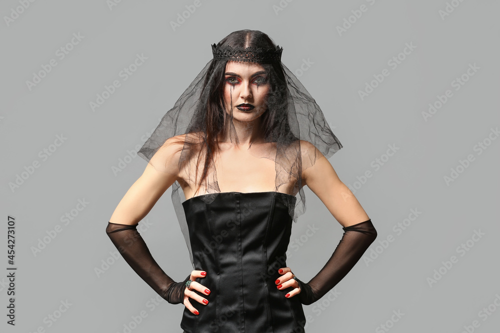 Beautiful woman dressed as witch for Halloween on grey background Beautiful woman dressed as witch for Halloween on grey background