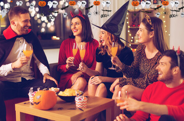 friendship, holiday and people concept - group of happy smiling friends in halloween costumes of vampire, devil, witch and cheetah with non-alcoholic drinks at home party at night