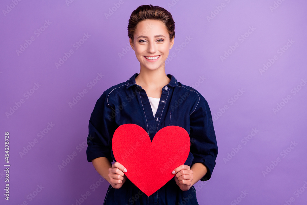 Photo of lovely young lady hold heart wear jeans overall isolated on violet color background Photo of lovely young lady hold heart wear jeans overall isolated on violet color background