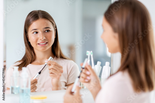 beauty, make up and cosmetics concept - teenage girl applying eye makeup with mascara and looking to mirror at home bathroom
