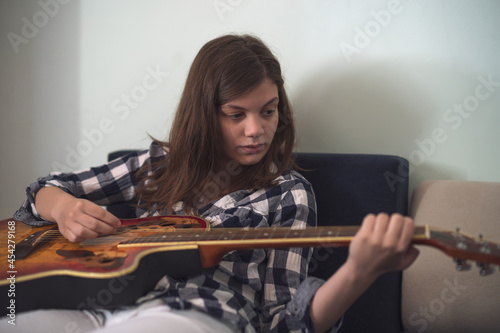 Teenage girl is playing guitar at home.