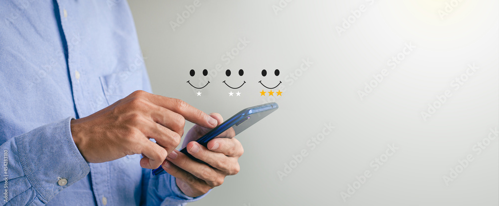 Customer Satisfaction Rating Concept A man holds a smartphone watching a performance on a scoring screen with a three-star gold symbol and a smiling face to her satisfaction. - obrazy, fototapety, plakaty 