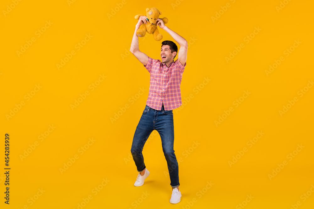 Full body photo of positive happy man raise bear toy good mood look empty space isolated on yellow color background