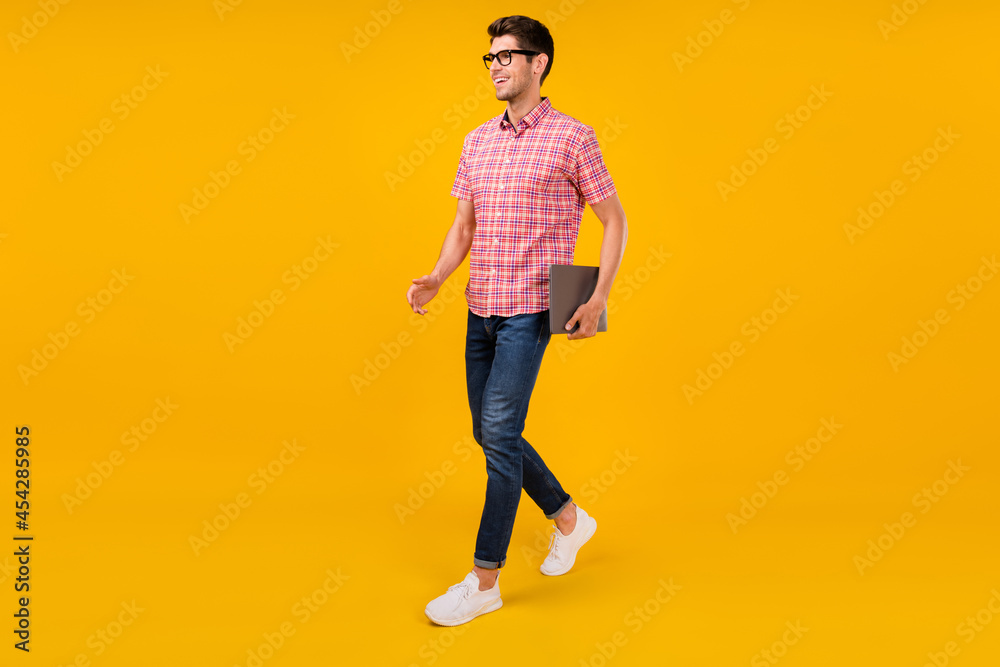 Full length body size view of attractive cheerful guy going holding laptop isolated over bright yellow color background Full length body size view of attractive cheerful guy going holding laptop isolated over bright yellow color background
