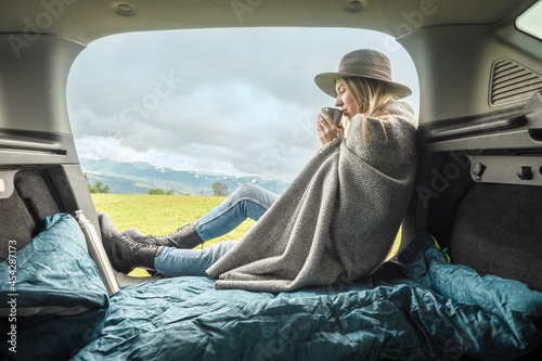 Girl resting in her car. Woman traveler camper relaxing, drinking hot tea on top of mountain. Road trip. Health care, authenticity, sense of balance.