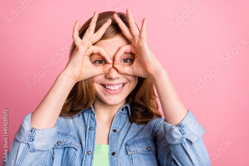 Photo portrait girl smiling showing okay fingers watching in binocular isolated pastel pink color background