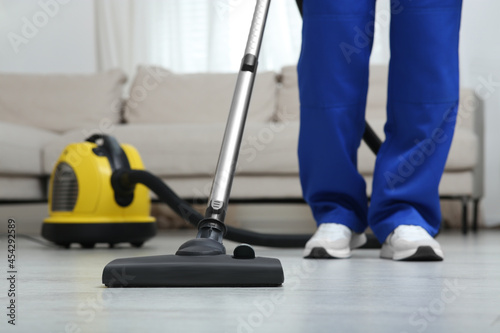 Janitor in uniform vacuuming floor indoors, closeup