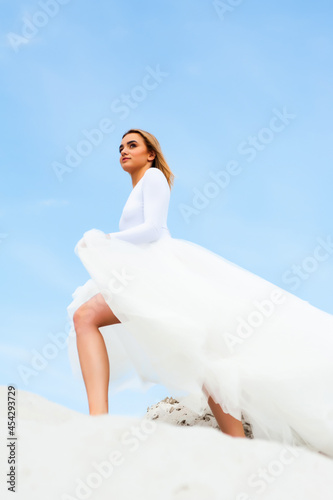 Bride in white dress outdoor on the sand and blue sky background