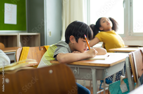 Unhappy Schoolboy studying in classroom at school during lesson, bored and discouraged student. School children education habit concept.