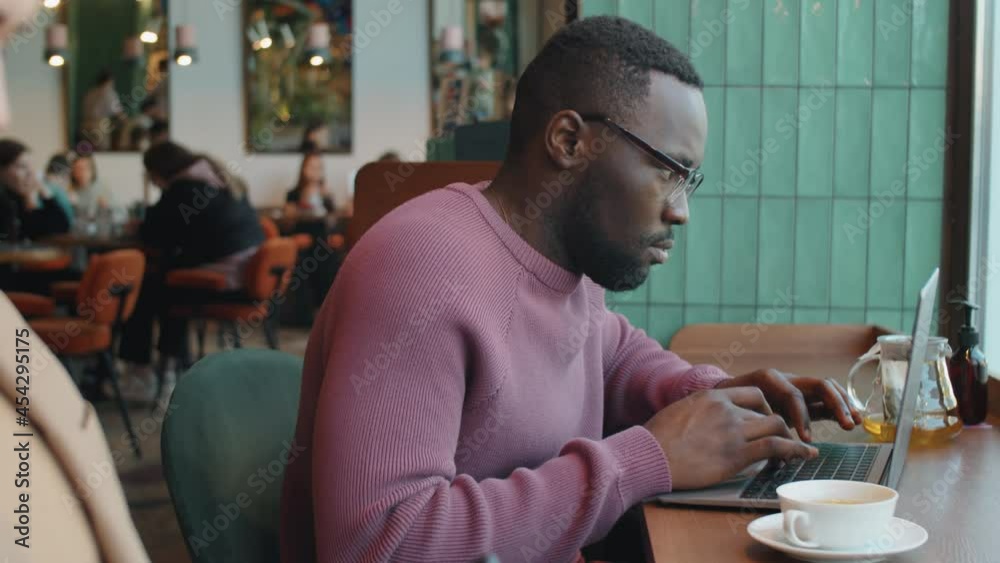 Young Afro-American businessman sitting at bar table by window in cafe and working on laptop Young Afro-American businessman sitting at bar table by window in cafe and working on laptop
