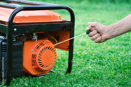 Hand starts a portable gasoline electric generator standing on the green grass