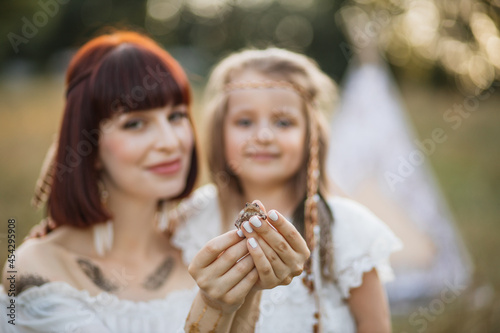 Close up small frog in hands of beautiful young woman. Blurred view of smiling mother and cute daughter, posing at camera and happy to meet little frog in the summer field. Focus on the frog