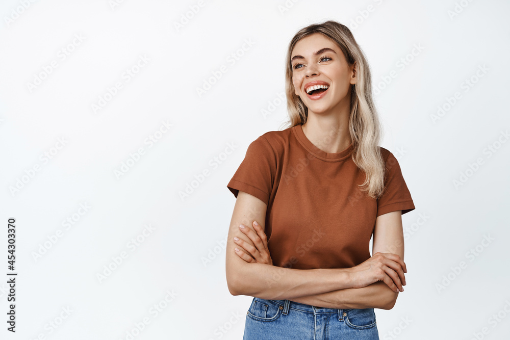 Happy laughing girl looking aside, cross arms on chest and smiling, looking at logo or advertisement, standing in tshirt over white background Happy laughing girl looking aside, cross arms on chest and smiling, looking at logo or advertisement, standing in tshirt over white background