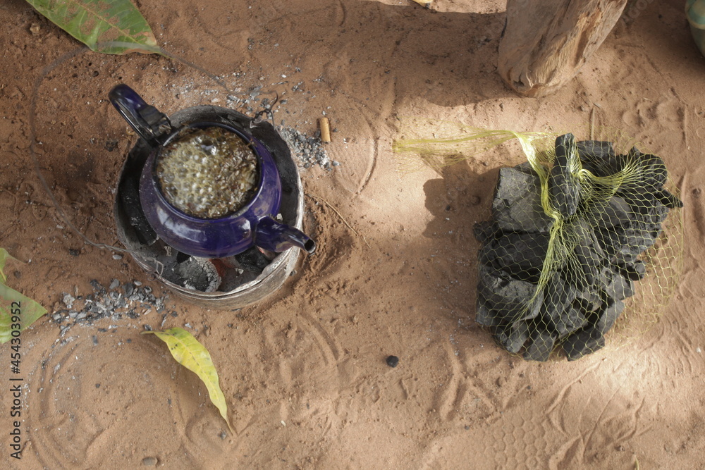 object closeup : aerial horizontal photography of a small blue kettle standing on a burning coal, with attaya tea boiling inside, outdoors on a sunny day in the Gambia, Africa