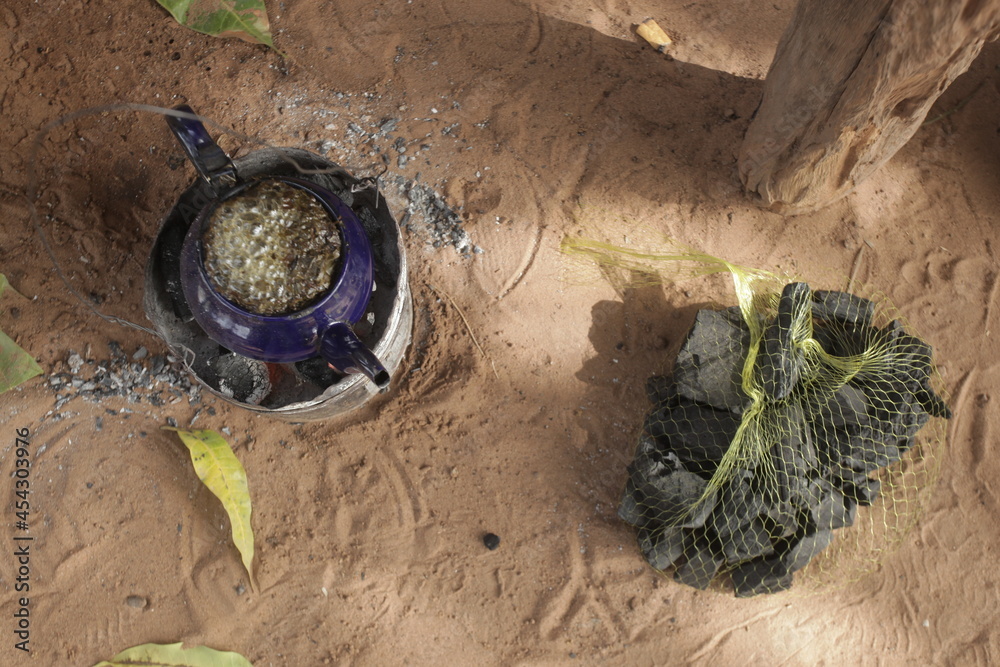 object closeup : aerial horizontal photography of a small blue kettle standing on a burning coal, with attaya tea boiling inside, outdoors on a sunny day in the Gambia, Africa