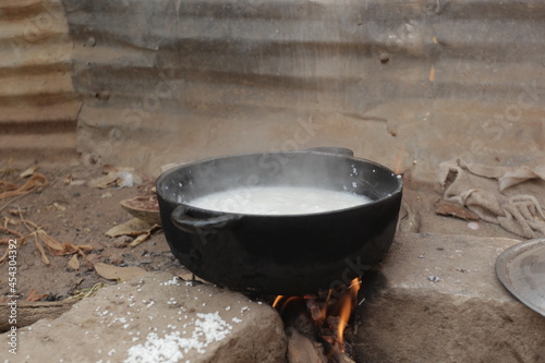 Obraz na płótnie horizontal photography of a black metal pot with rice boiling inside, standing on three concrete bricks over burning wood fire, outdoors in the Gambia, Africa w salonie