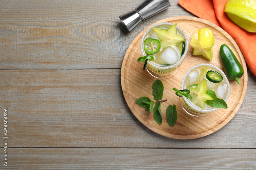 Glasses of spicy cocktail with jalapeno, carambola and mint on wooden table, flat lay. Space for text Glasses of spicy cocktail with jalapeno, carambola and mint on wooden table, flat lay. Space for text