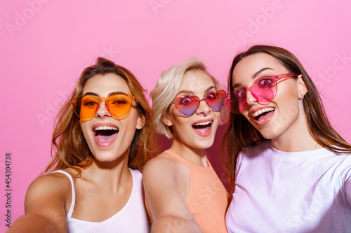 Self portrait of three funny, funky, emotional, expressive, pretty girls, gesture posing on pink background, celebrating birthday, women's day, spring