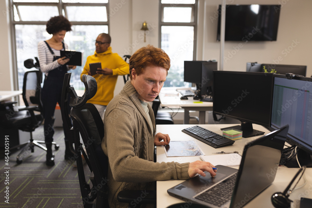 Caucasian male creative at work, sitting at desk, using laptop Caucasian male creative at work, sitting at desk, using laptop