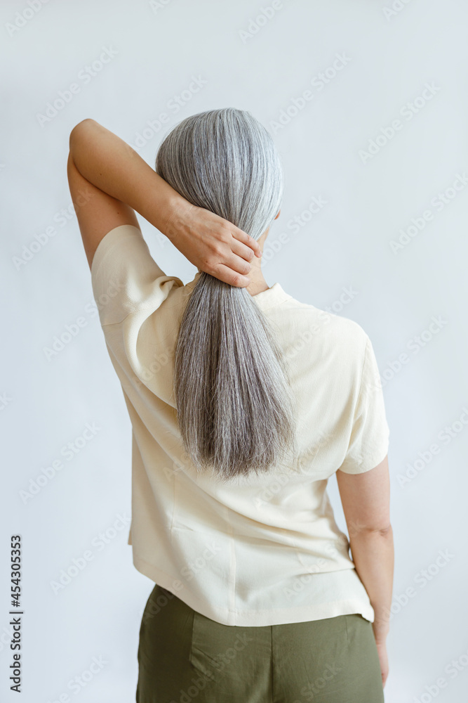 Elegant woman in yellow shirt makes polytail of long silver hair ...