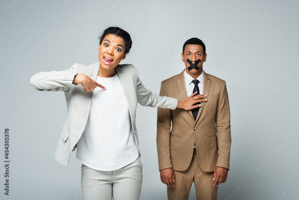 arrogant african american businesswoman pointing at herself and pushing away manager with scotch tape on mouth isolated on grey arrogant african american businesswoman pointing at herself and pushing away manager with scotch tape on mouth isolated on grey