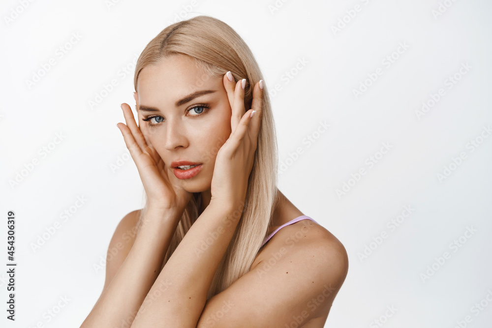 Skin care. Close up portrait of blond attractive woman, touching her face near eyes, looking sensual at camera, concept of cosmetic products and spa, white background Skin care. Close up portrait of blond attractive woman, touching her face near eyes, looking sensual at camera, concept of cosmetic products and spa, white background