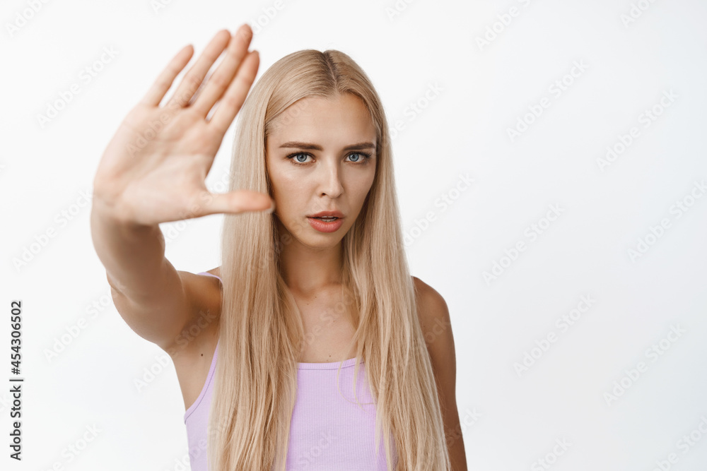 Serious young woman asking to stop filming her, showing no, rejection gesture, refusing and say no, standing over white background Serious young woman asking to stop filming her, showing no, rejection gesture, refusing and say no, standing over white background