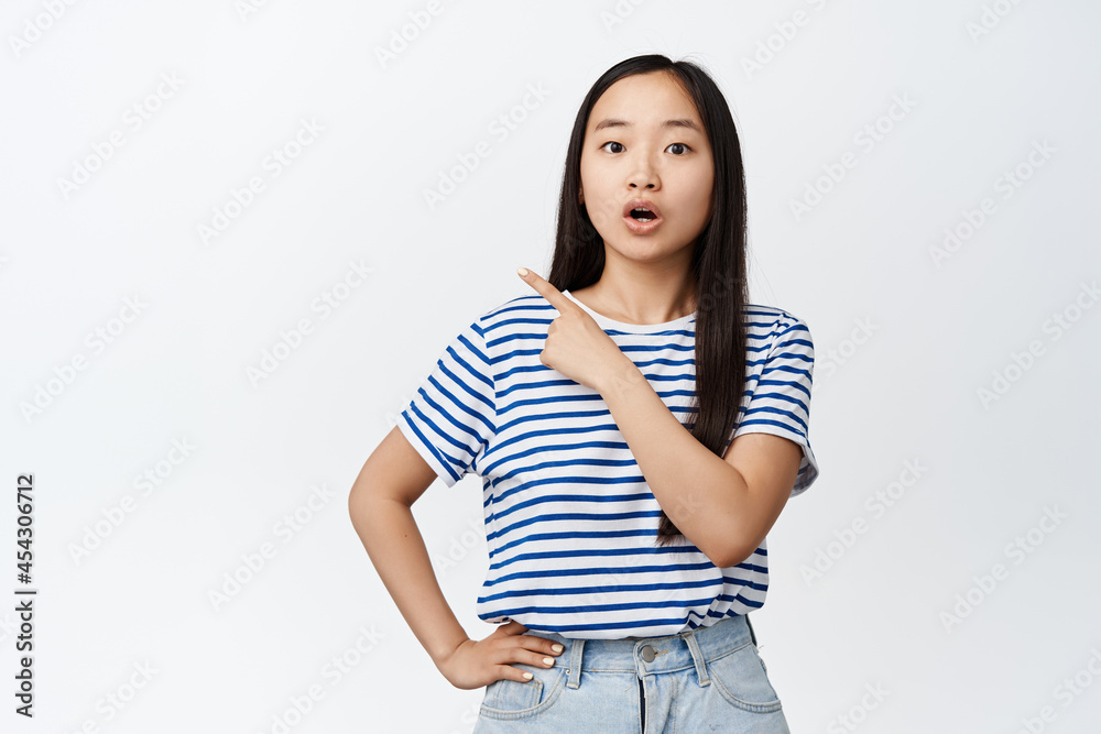 Portrait of asian girl say wow, looking surprised and amazed by something, showing advertisement, acting curious, standing against white background Portrait of asian girl say wow, looking surprised and amazed by something, showing advertisement, acting curious, standing against white background