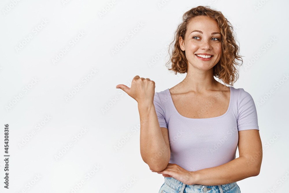 This way. Attractive blond girl pointing finger left and smiling, showing announcement, advertising something, standing over white background