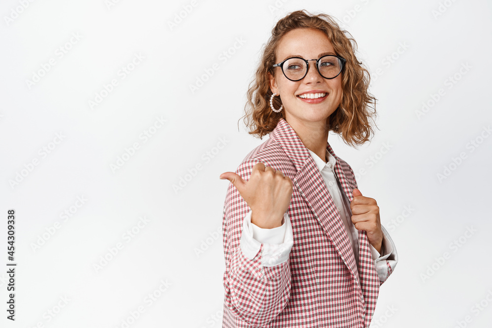 Stylish female entrepreneur in glasses and suit, smiling and showing something, pointing finger at company logo, left side copy space, white background Stylish female entrepreneur in glasses and suit, smiling and showing something, pointing finger at company logo, left side copy space, white background