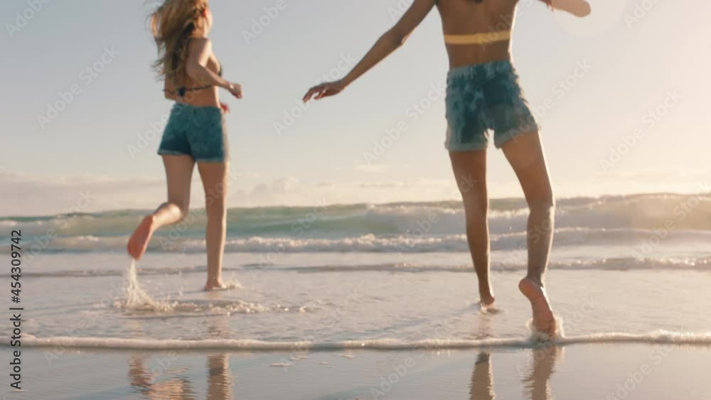 two women on beach splashing sea water at each other having fun teenage girls playing game on warm summer day by the ocean enjoying summertime holiday vacation