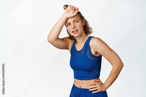 Young sportswoman wipe sweat on forehead, looking back after running, finish jogging training session. Female fitness woman tired after workout, white background