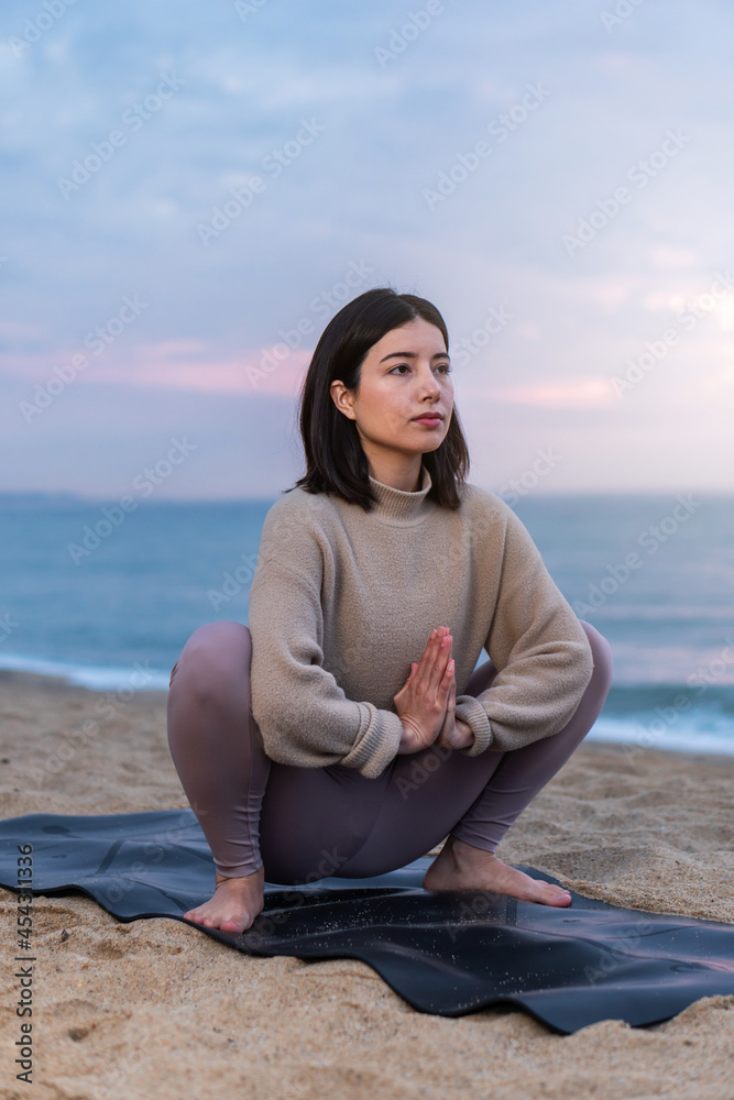 Woman doing yoga at the beach at sunrise