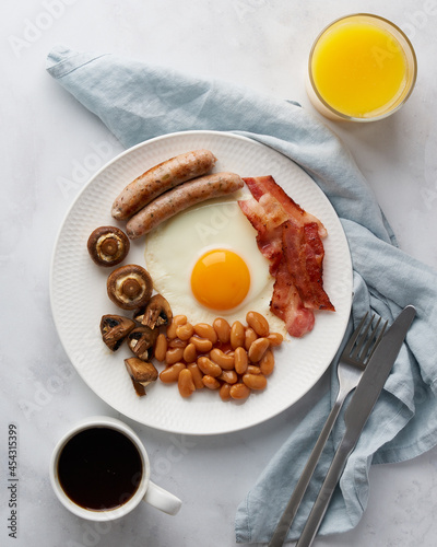 Delicious english breakfast. Tasty mushrooms, fried egg yolks, kidney beans, grilled sausages, smoky bacon, fresh orange juice, hot cup of coffee. Ketogenic meal on white background