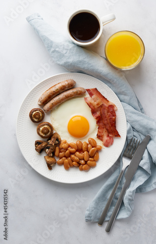 Vertical of delicious irish breakfast. Classic irish cuisine on white plate. Fried eggs, grilled sausages, smoky bacon, beans, mushrooms, coffe and orange juice. Top view of ketogenic food