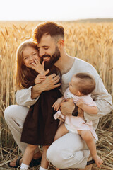 Happy young father in the arms of his little daughters. Dad and 2 daughters are photographed in the field, a happy Ukrainian family