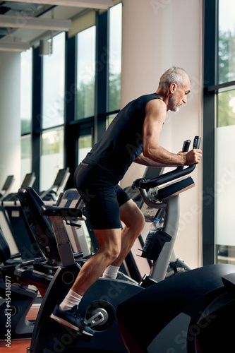 Mature athletic man during sports training on stationary bike in gym. © Drazen