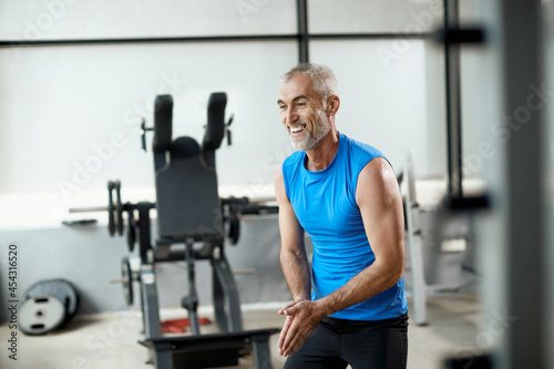 Happy mature sportsman prepares for lifting barbell while working out in gym.
