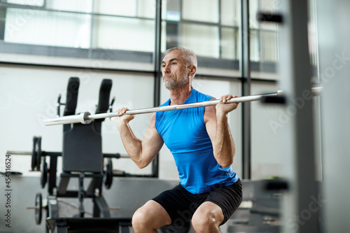 Mature athlete exercises with barbell during weight training in gym.