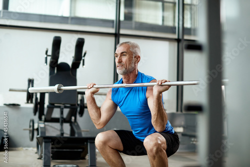 Mature sportsman exercises strength while lifting barbell in gym.