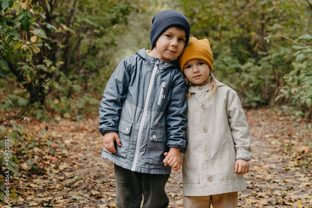 brother and sister on a walk: the older boy and the younger girl take a walk together in the autumn park brother and sister on a walk: the older boy and the younger girl take a walk together in the autumn park
