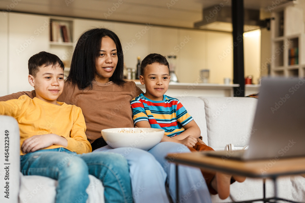 Two boys and their mother watching movie on laptop while eating popcorn Two boys and their mother watching movie on laptop while eating popcorn