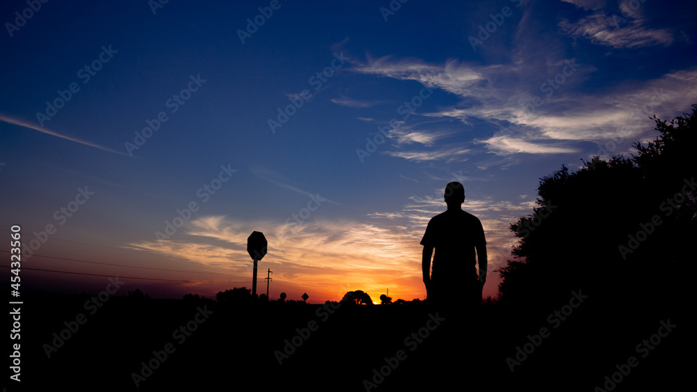 Silhouette of a man on a road watching the sunset. Concept of traveling on vacation.