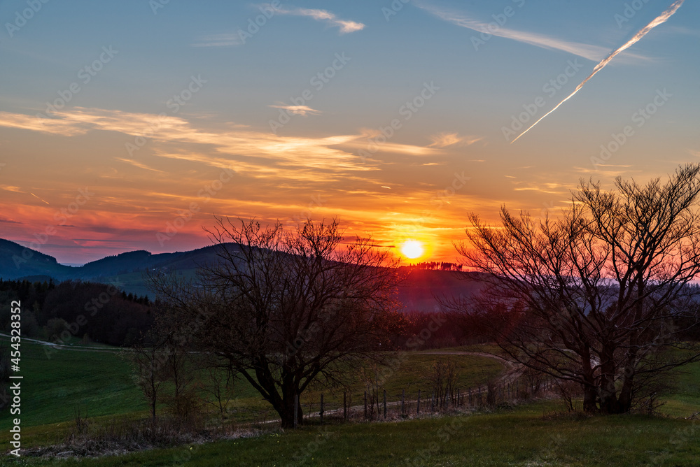Sunset in mountains with hills, colorful sky, trees and meadows