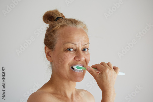 Mature woman brushing teeth with toothbrush as healthy morning routine