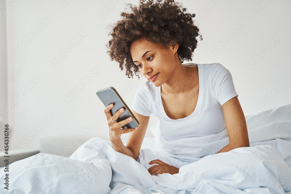 Female with a smartphone in her hand sitting in bed