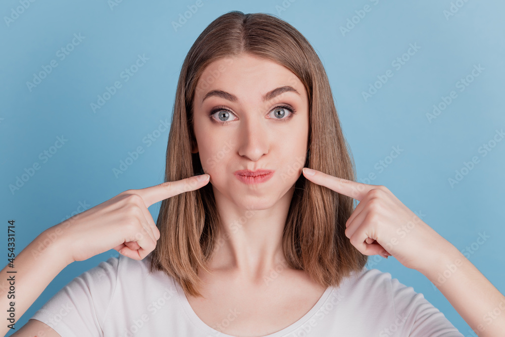 Portrait of funny childish girl press fingers puffed cheeks on blue background Portrait of funny childish girl press fingers puffed cheeks on blue background